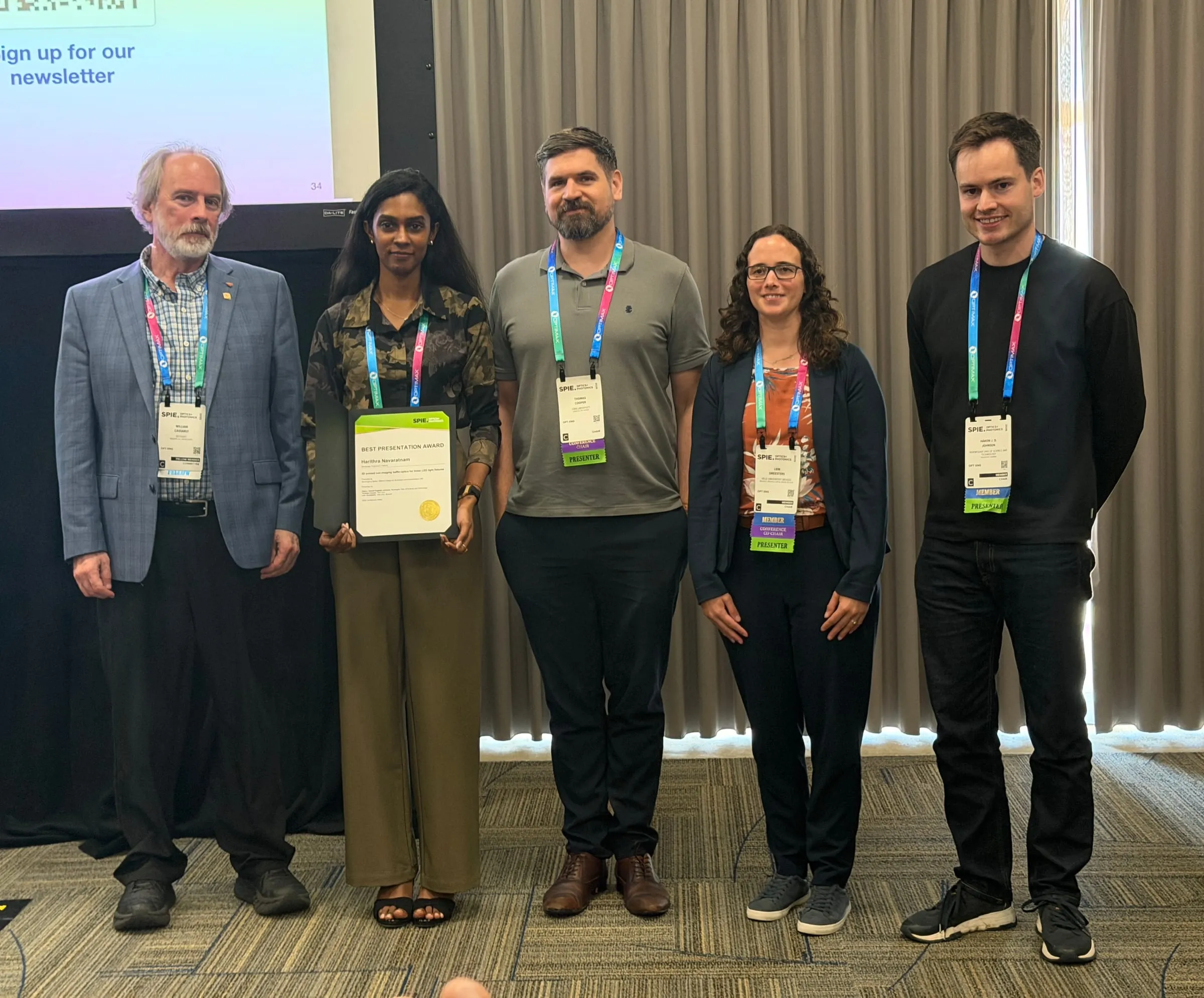 Harithra Navaratnam holding her Best Student and Postdoc Presentation Award alongside Bill Cassarly and conference chairs Thomas Cooper, Lien Smeesters, and Håkon J. D. Johnsen